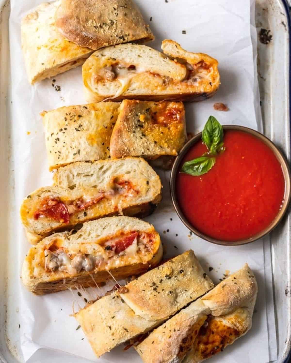 Stromboli on a cookie sheet with a bowl of pizza sauce.