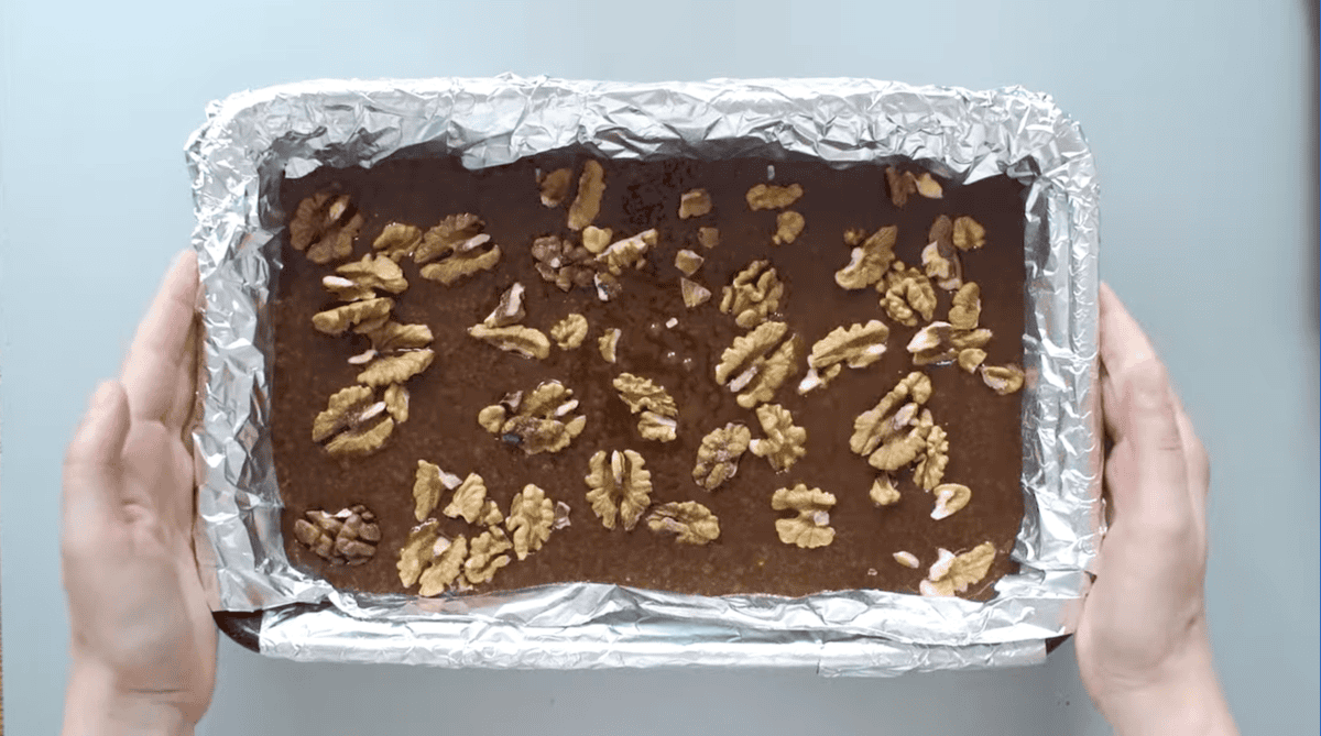 homemade brownie batter topped with nuts in foil-lined baking pan.