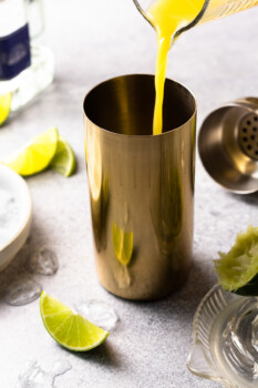 orange juice being poured into a metal cocktail shaker.