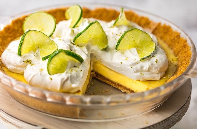 key lime pie topped with whipped cream and lime slices on a cake stand