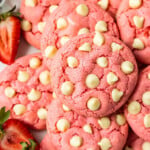Pink strawberry cookies with white chocolate chips and strawberries on a plate.
