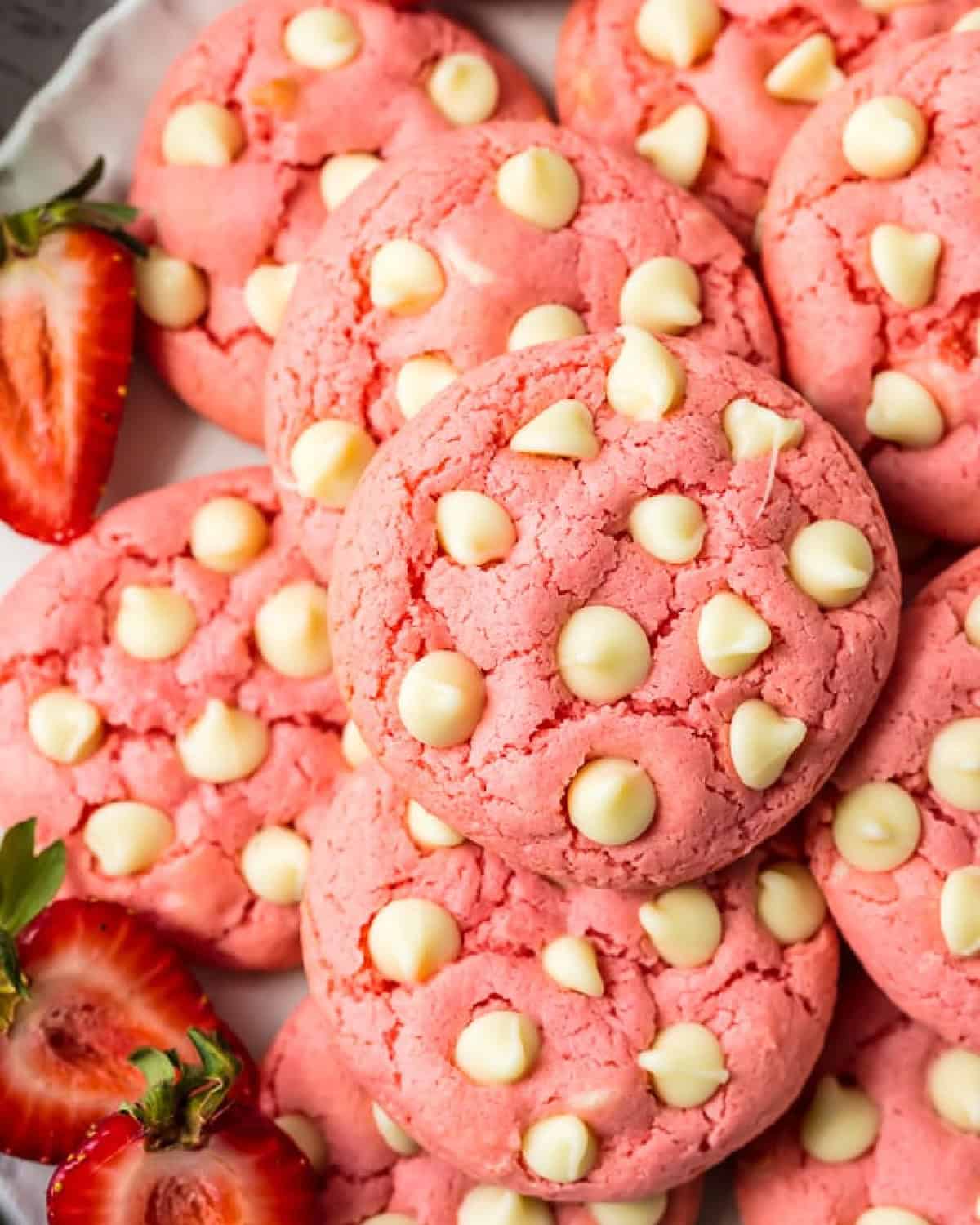 Pink strawberry cookies with white chocolate chips and strawberries on a plate.