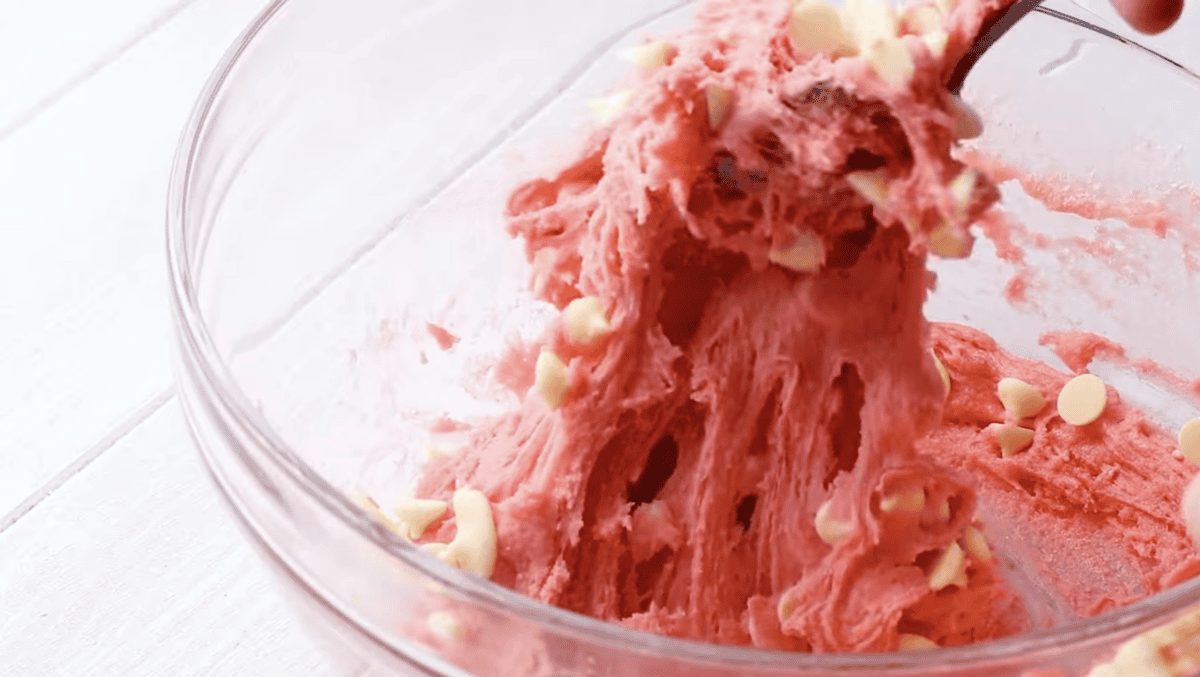 pink cookie dough in a glass bowl with white chocolate chips.