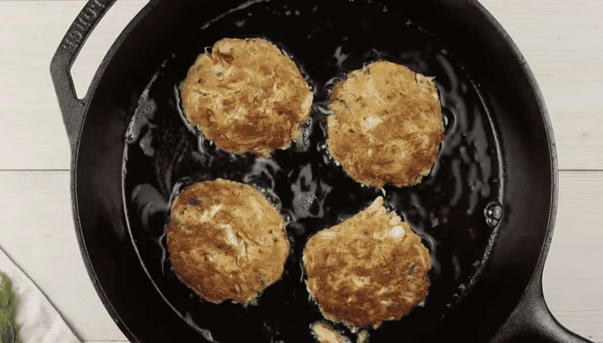 4 crabcakes cooking in a black skillet. 