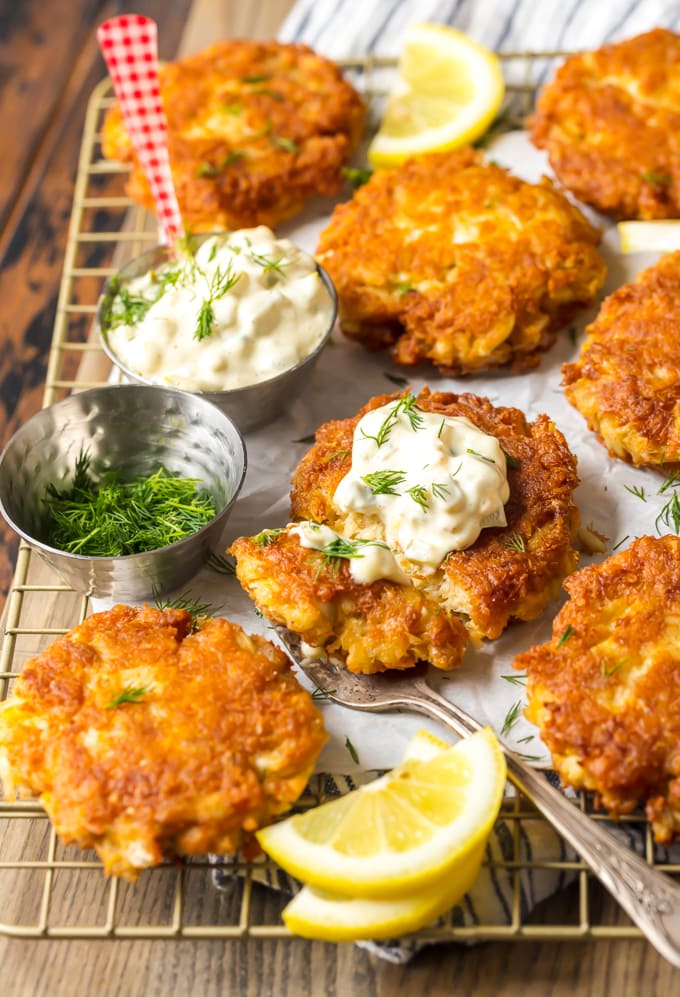 Crab cake patties arranged on a cooling rack, with small bowls of dill and tartar sauce