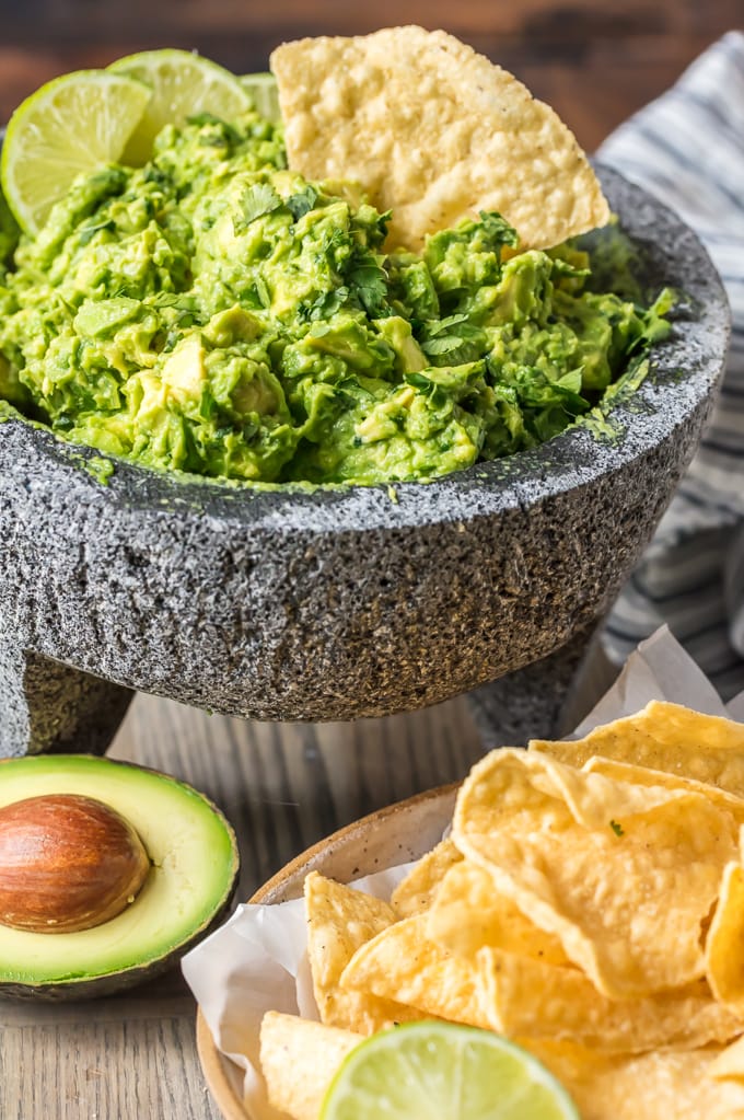 Homemade guacamole dip in a mortar & pestle, with a single tortilla chip dipped in