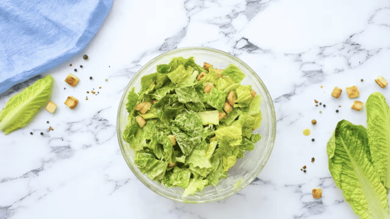 A caesar salad with croutons on a marble table.