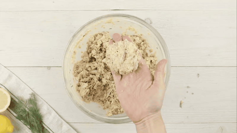 a hand holding a shaped crab cake over a bowl of crab cake meat.