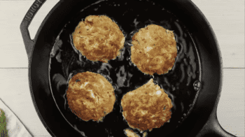 4 crab cakes cooking in a cast iron skillet.