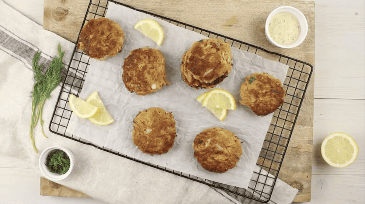 6 crab cakes on a cooling rack with lemon wedges and tartar sauce.