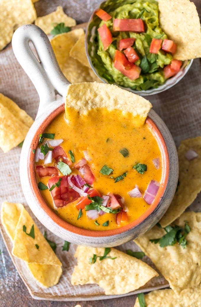 Healthy Queso is an amazing and EASY Skinny Cheese Dip Recipe that has less fat and less calories than a typical queso dip recipe. We made this healthy cheese dip with coconut milk and greek yogurt to keep things low cal while not sacrificing flavor or texture. This is our favorite healthy Cinco de Mayo Appetizer recipe! queso dip and guacamole on a plate with chips
