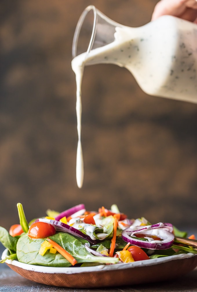 Homemade ranch dressing being poured onto a colorful salad