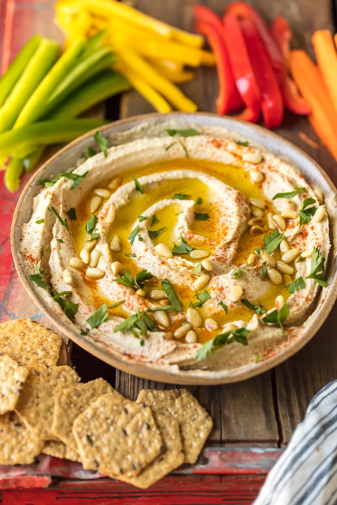 A bowl of homemade hummus next to colorful peppers and crackers