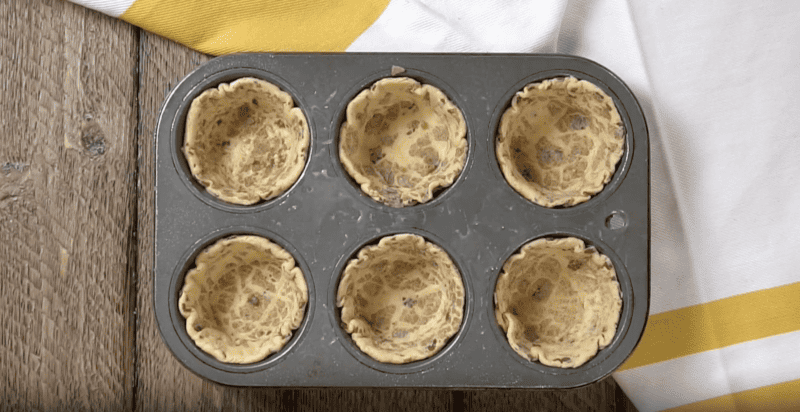 a muffin tin with 6 flattened cinnamon rolls pressed into it.