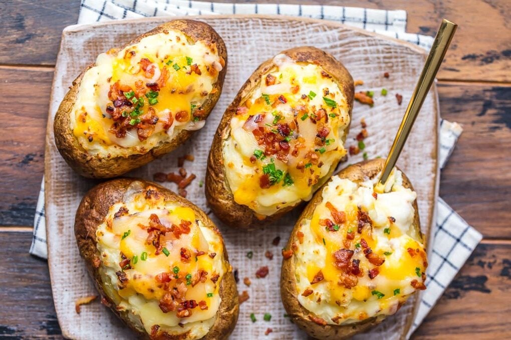 A plate of four twice baked potatoes topped with cheese and bacon.