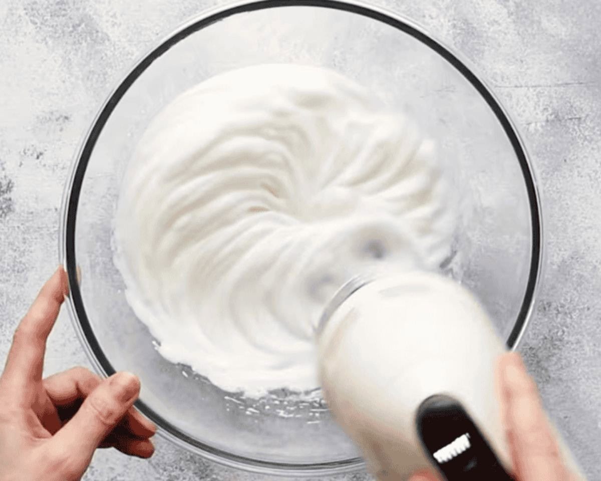 Whipping egg whites with a hand mixer in a glass bowl.