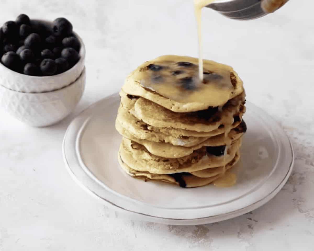 Creamy lemon syrup being drizzled over the top of a stack of pancakes.