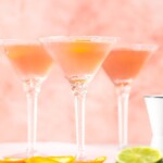 three glasses with cosmos inside beside a cut lime