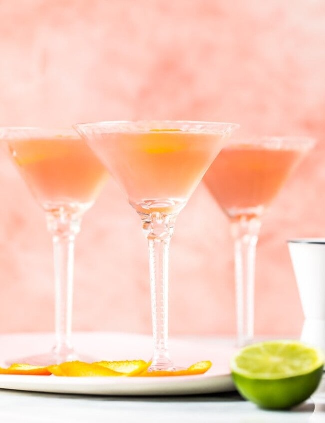 three glasses with cosmos inside beside a cut lime