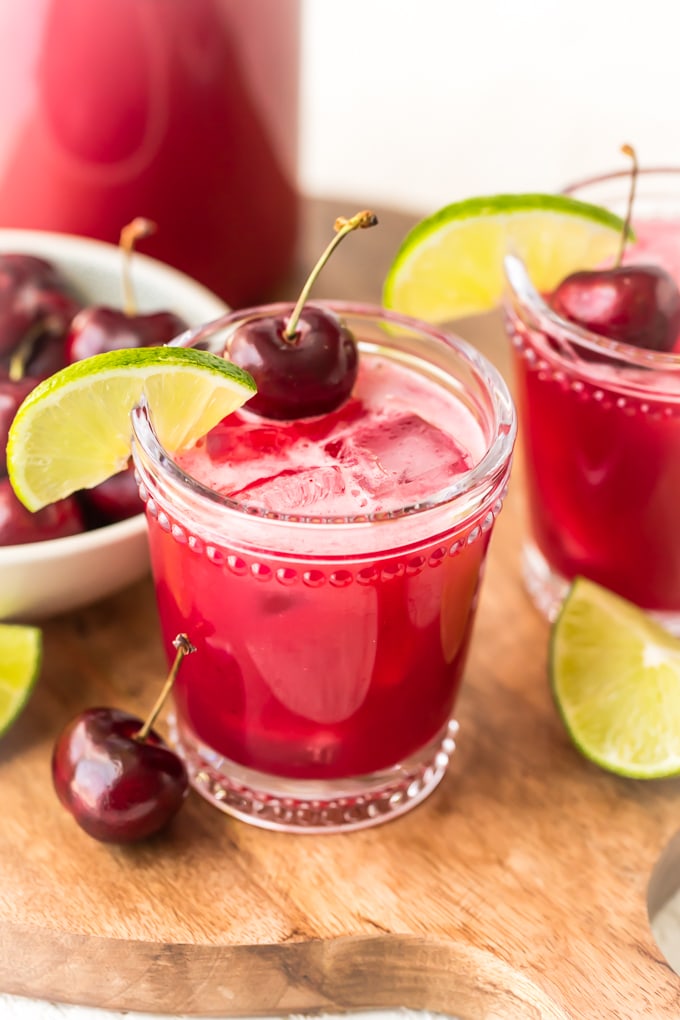 Two glasses of cherry limeade on a wooden cutting board.