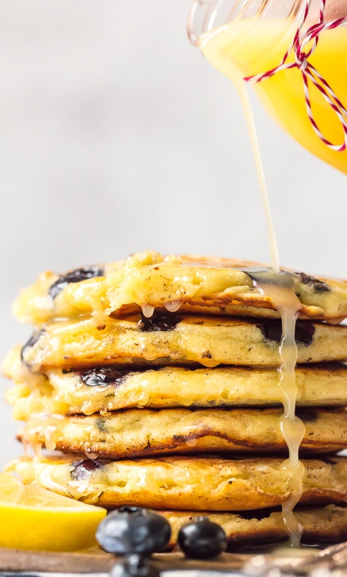 Homemade lemon sauce pouring over a stack of blueberry pancakes