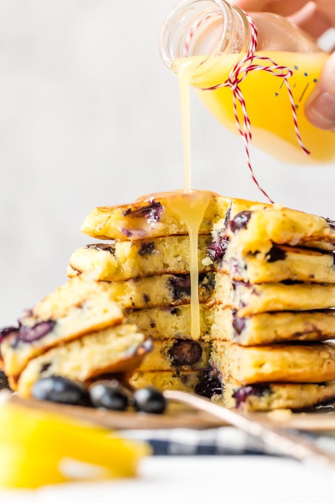 Lemon sauce being poured over a stack of blueberry pancakes