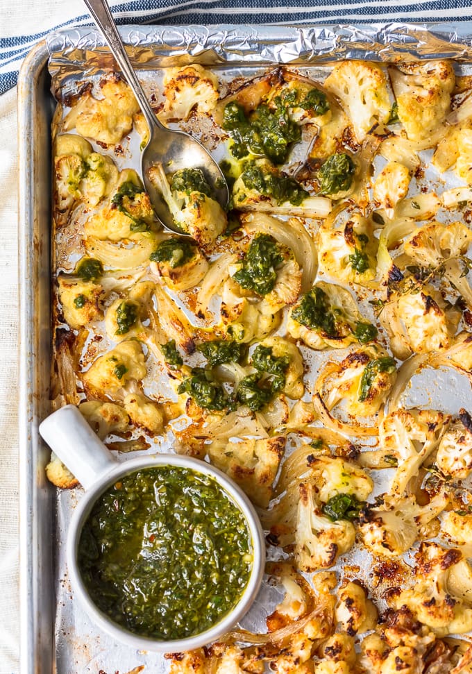 Baking tray with roasted cauliflower, onion, garlic, and chimichurri sauce