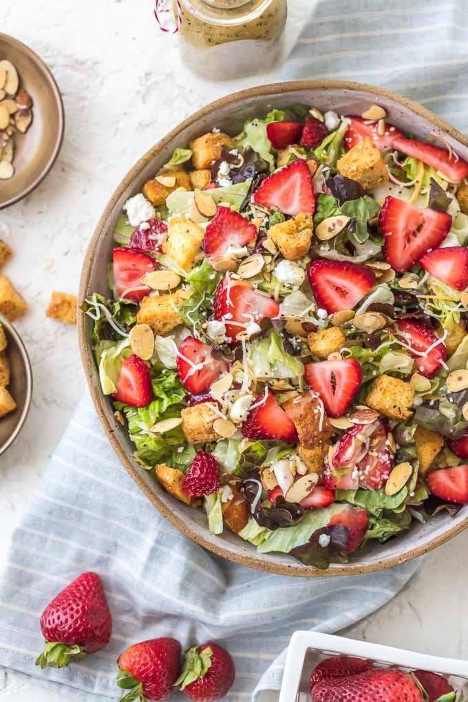 Big bowl of salad filled with strawberries, feta, lettuce, almonds, and croutons