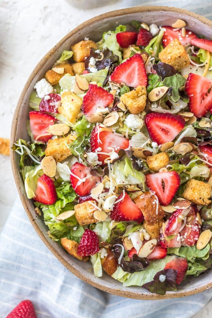 Strawberry Salad with Poppy Seed Dressing is a fresh, fun, and fruity salad! This healthy Strawberry Poppy Seed Salad is our fave summer salad recipe is filled with all kinds of good stuff, like lettuce, almonds, feta cheese, homemade croutons, and fresh strawberries. I even topped it off with my very own homemade Poppy Seed Dressing recipe! I'm going to be making this tasty summer salad all season long for a fresh and healthy lunch. Strawberry Poppyseed Salad topped with fresh strawberries, croutons, feta, and more