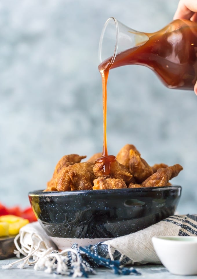 Sweet and sour chicken sauce being poured over a bowl of chicken