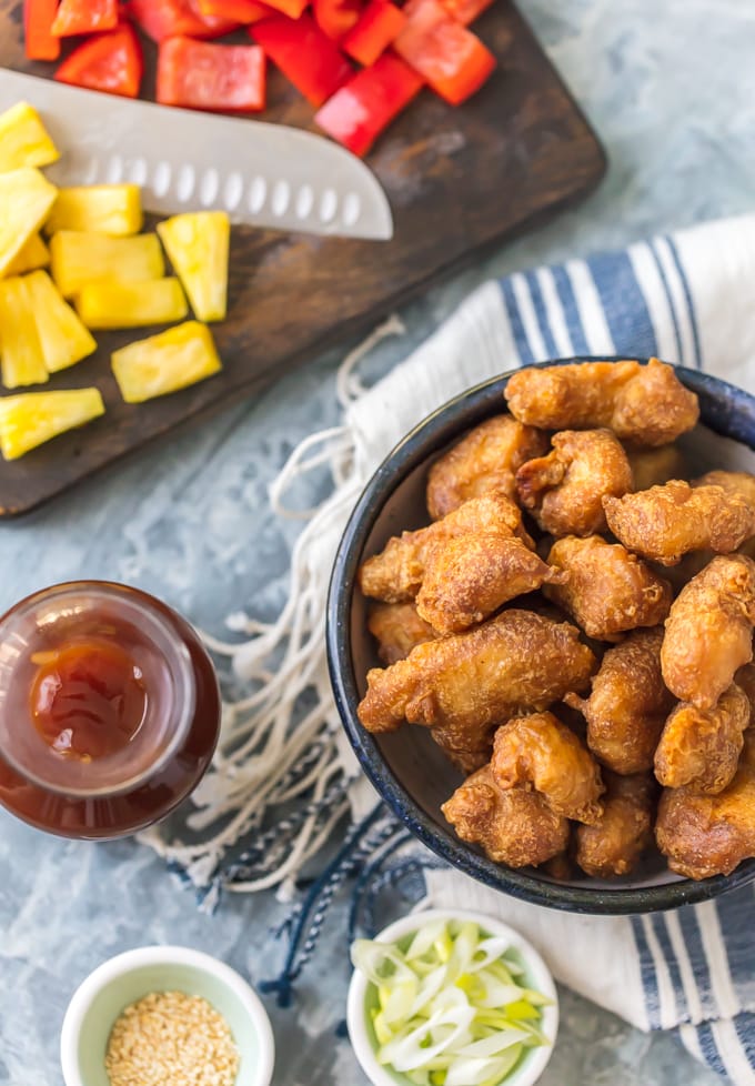 A bowl of sweet and sour chicken next to a cutting board with chopped pineapple and peppers