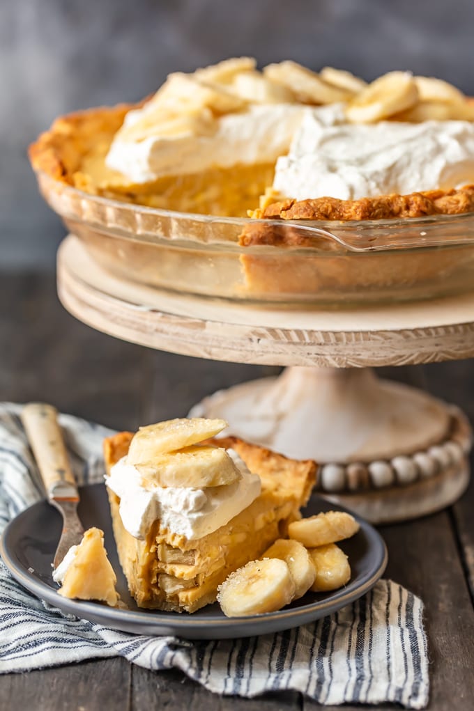 A slice of pie on a plate in front of a pie on a pedestal