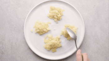 dividing chopped cooked onions into 4 equal portions on a white plate with a spoon.
