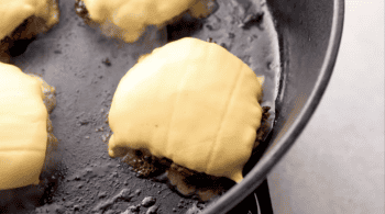 cheese melting over cooked hamburgers in a pan.