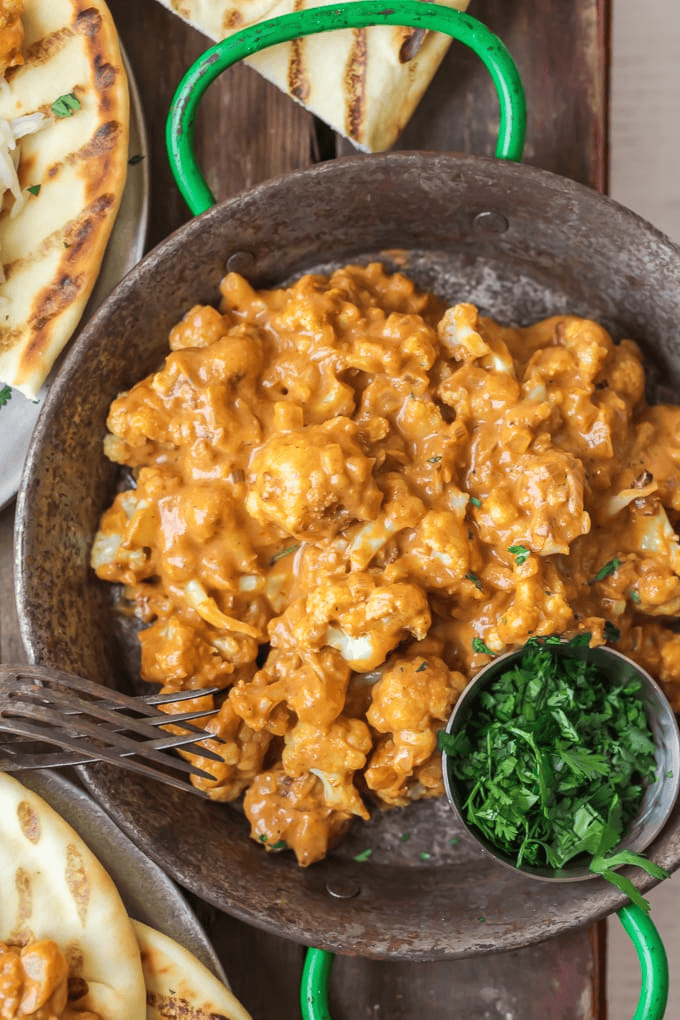 cauliflower tikka masala in a cast iron dish with a side of cilantro and naan in a dish.