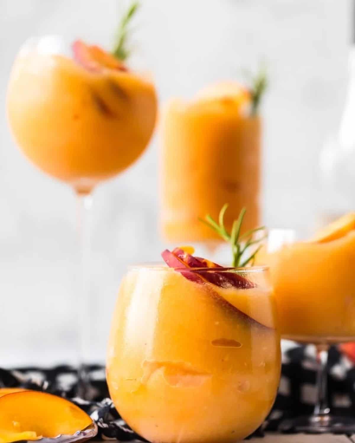 This Peach Frosé recipe is the perfect peachy summer cocktail! Frozen Rosé is icy, chill, and refreshing. Learn how to make frosé for all your summer occasions! Peach frose in serving glasses garnished with peaches and rosemary.