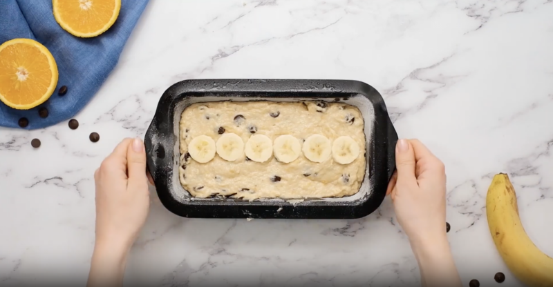 chocolate chip banana bread batter topped with banana slices in a loaf pan.