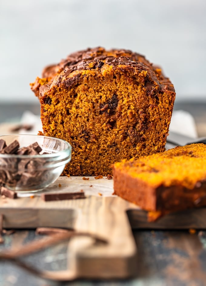 Chocolate chunk pumpkin bread on a cutting board, next to a bowl of chocolate chunks