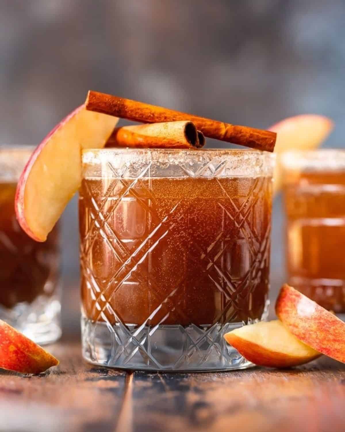 Apple butter old fashioned in a glass garnished with apple slices and a cinnamon stick.