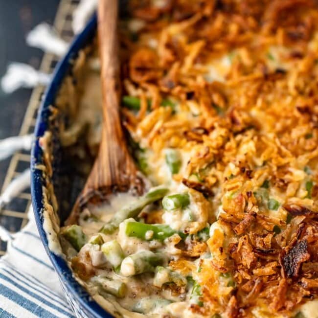 Cheesy classic green bean casserole in a blue dish with a wooden spoon.