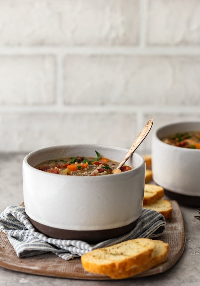 A white bowl of soup sitting on a dish towel, next to slices of bread