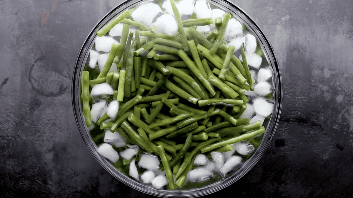 A refreshing serving of green beans in a glass bowl with ice cubes.