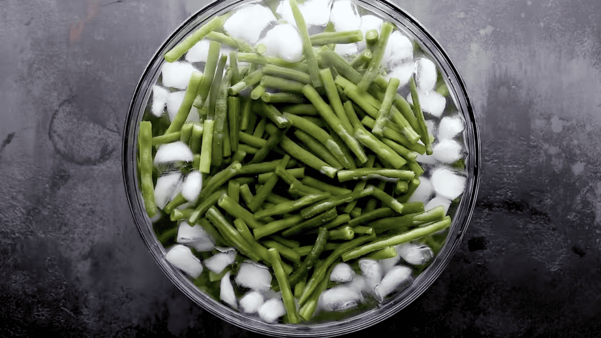 Green beans in a glass bowl filled with water and ice.