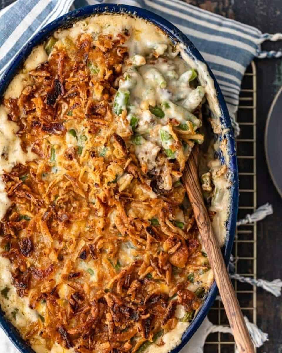 Classic Green Bean Casserole is one of those Thanksgiving recipes that you don't need to reinvent. It's absolutely perfect just the way it is, with green beans, cream of mushroom, crunchy fried onions, and some other awesome ingredients. This green bean casserole recipe is exactly what you need for you next holiday meal! A green bean casserole dish with a spoon on top.