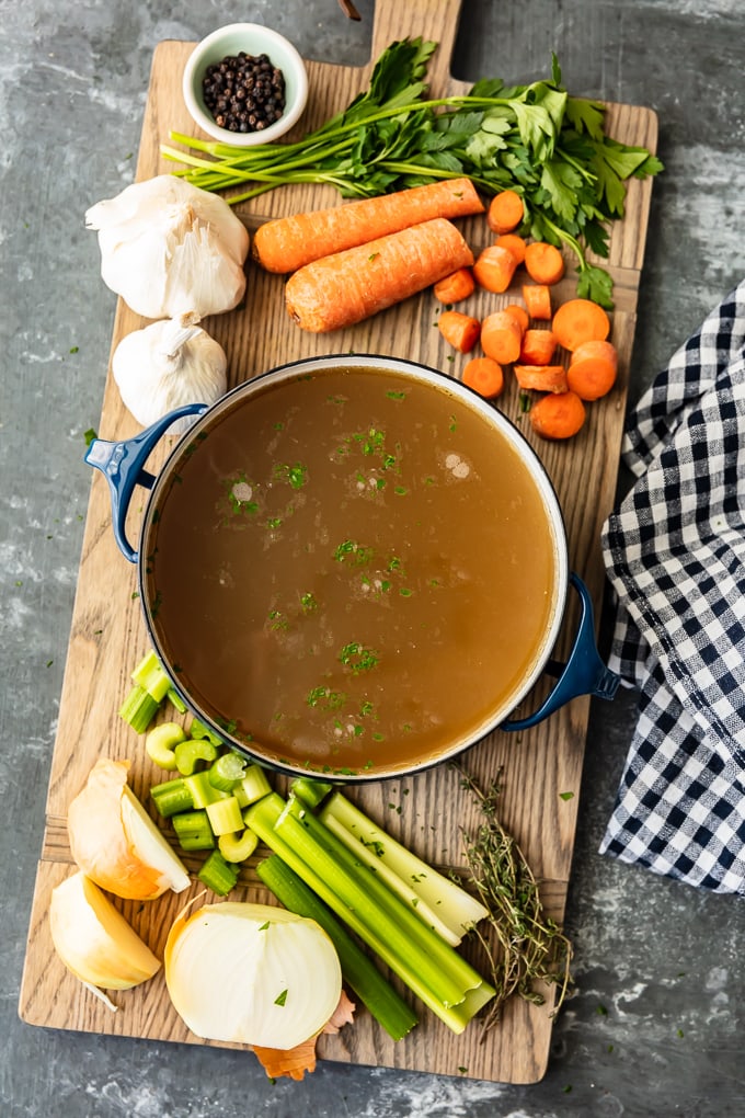 How to make chicken broth: carrots, celery, and garlic sit on a cutting board, next to a pot of chicken broth