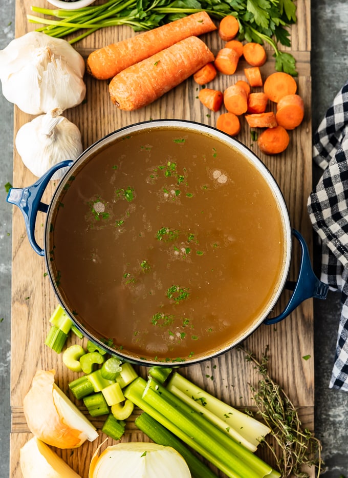 A pot of homemade chicken broth surrounded by carrots, garlic, and celery