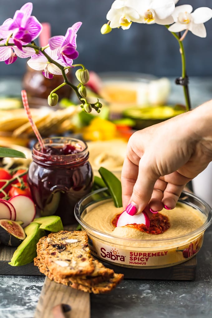 hand dipping sliced veggie into hummus