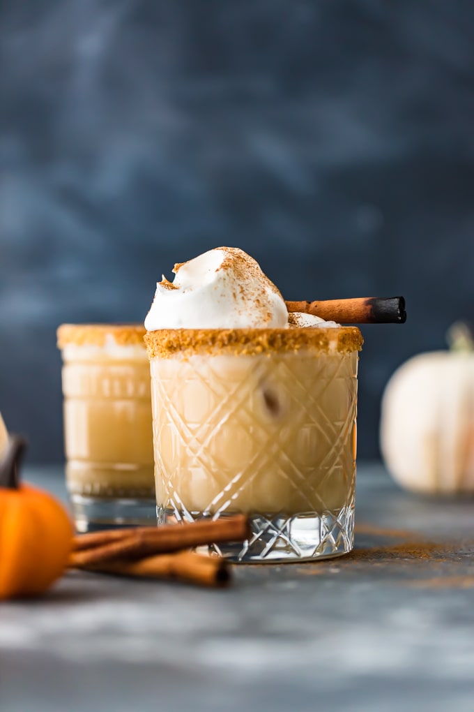 A White Russian cocktail with pumpkin spice flavoring and garnished with cinnamon sticks and whipped cream.