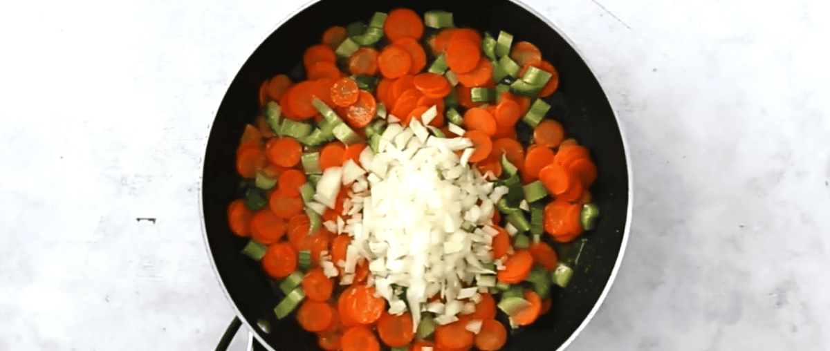 Adding the onion to a pot of carrots and celery