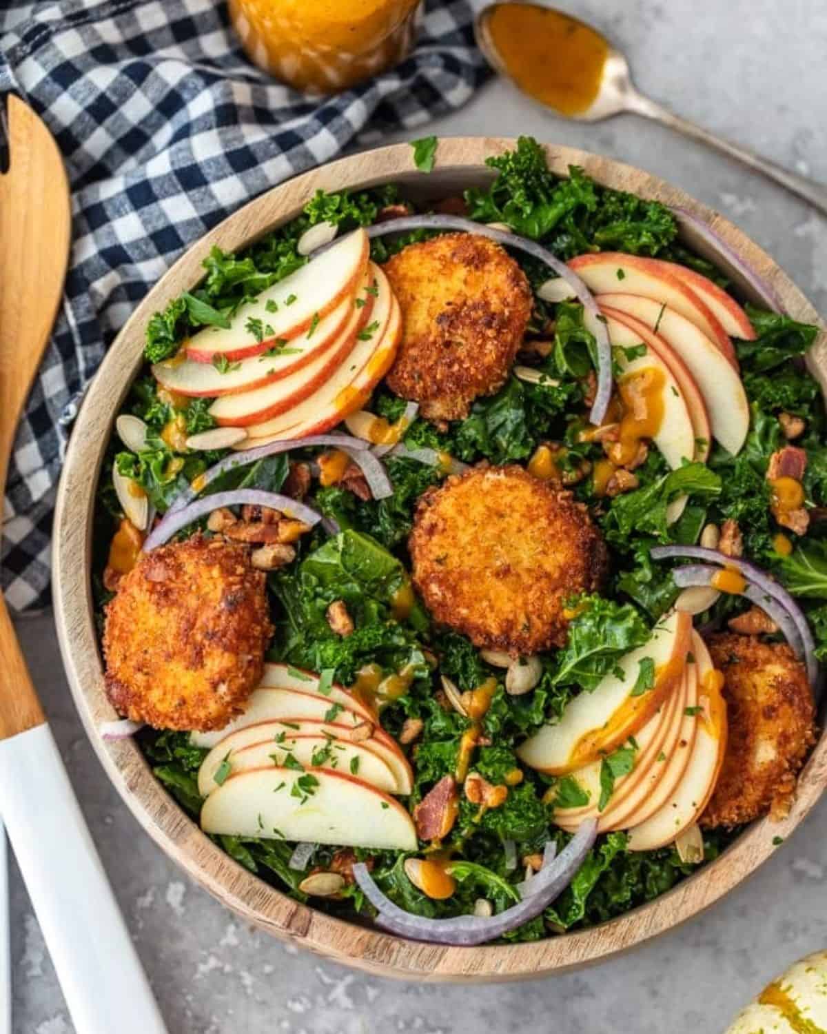 This Autumn Kale Salad recipe is the salad of the season! Made with kale, apples, onions, pumpkin seeds, bacon, fried goat cheese and a maple pumpkin salad dressing, it is the perfect fall salad idea. This delicious kale apple salad makes a tasty and healthy meal you'll want to eat all season long! Kale salad with fried goat cheese, red onions, apples, pumpkin seeds, bacon, and pecans.